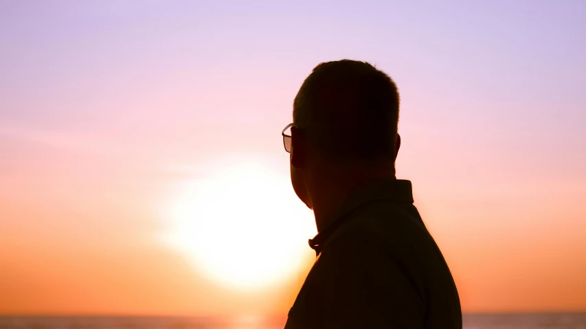 a man standing on top of a beach next to the ocean, pexels contest winner, sunset glow around head, profile image, man with glasses, middle aged man