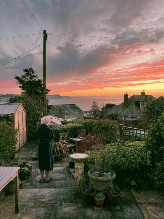 a woman standing on top of a wooden deck, an album cover, by Andrew Allan, pexels contest winner, fantastic realism, sunset panorama, shot from roofline, seaview, photography of gregory crewdson