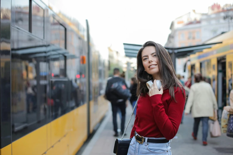 a woman standing in front of a yellow bus, pexels contest winner, happening, red sweater and gray pants, trams ) ) ), avatar image, brunette woman