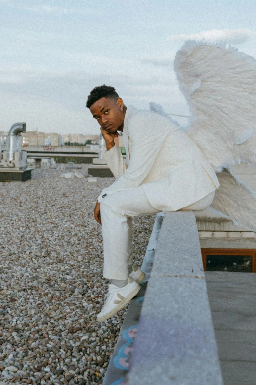 a man in a white suit sitting on a ledge, an album cover, by Cosmo Alexander, pexels contest winner, renaissance, winged boy, xxxtentacion, wide open wings, pose 4 of 1 6