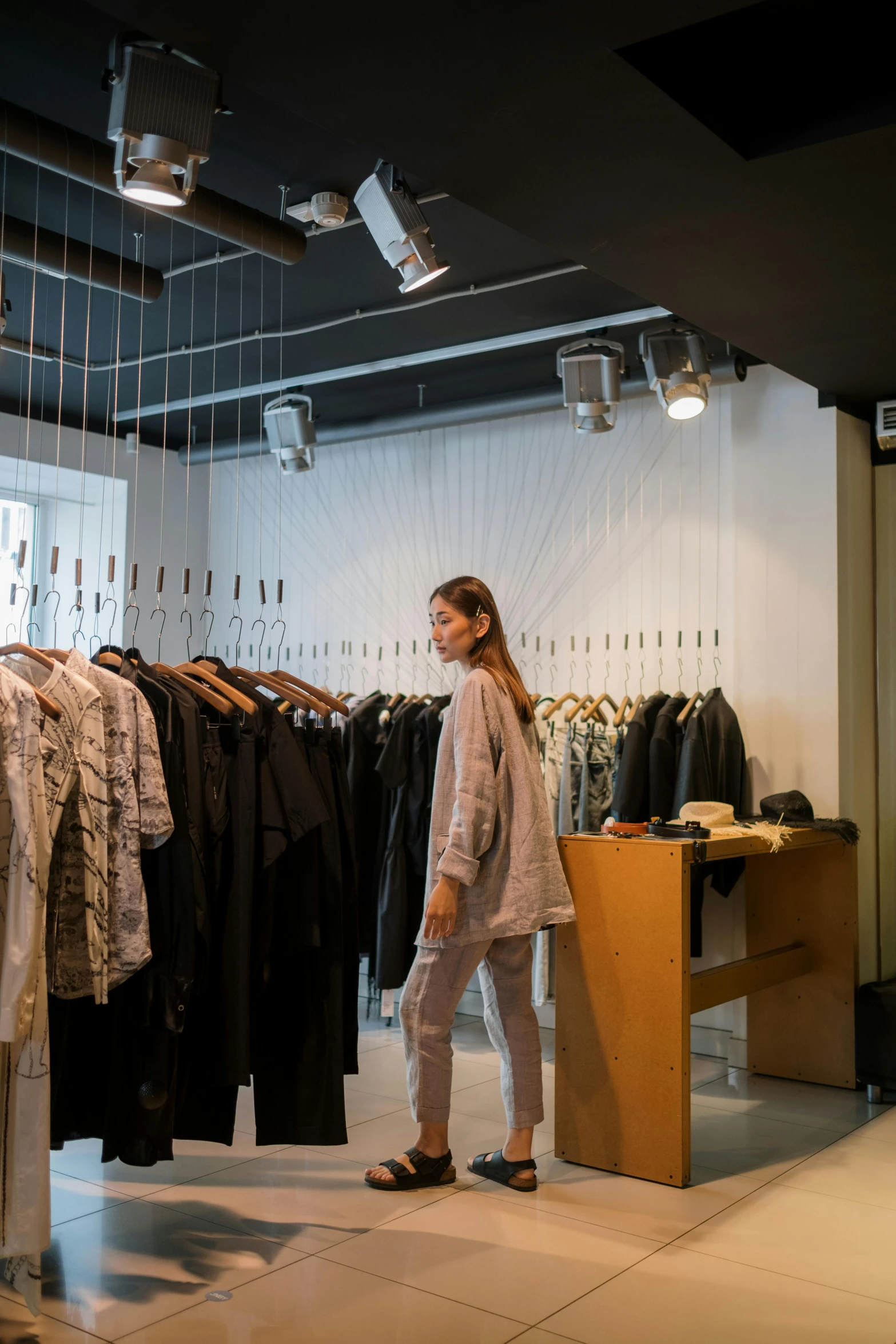 a woman standing in front of a rack of clothes, by Nina Hamnett, trending on unsplash, things hanging from ceiling, kirsi salonen, inspect in inventory image, official store photo