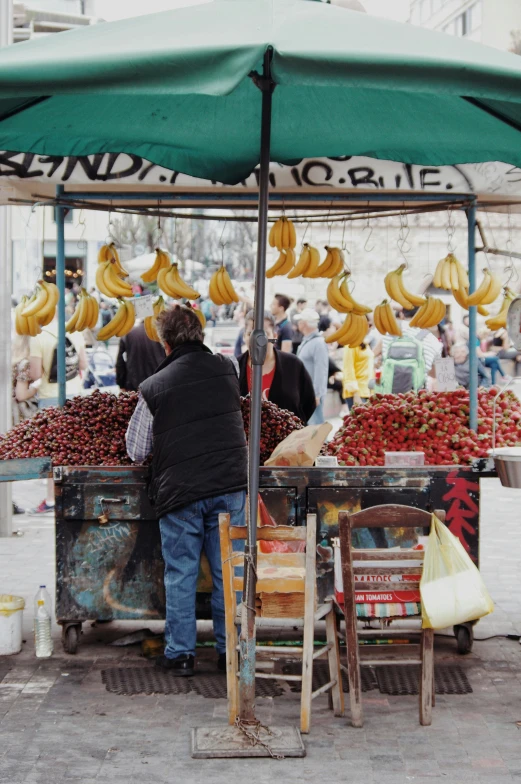 a man standing in front of a fruit stand, istanbul, facing away from camera, square, banana