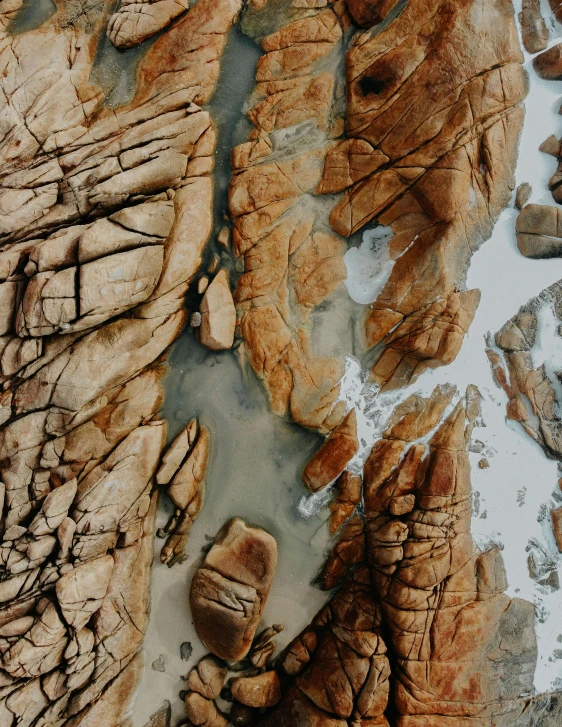 a bird's eye view of some rocks and water, an ultrafine detailed painting, trending on pexels, sandstone, glaciers, cracks, low quality photo