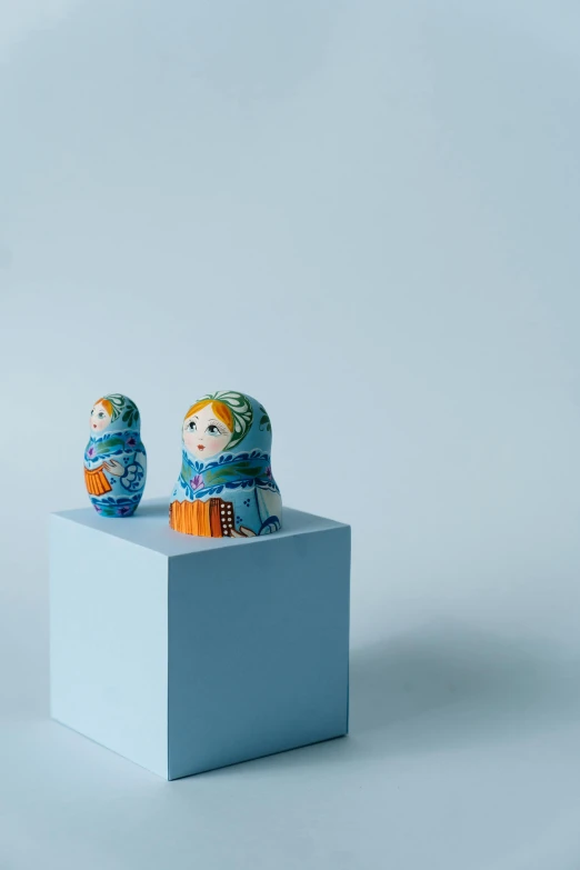 a couple of dolls sitting on top of a white box, unsplash, folk art, orange and cyan paint decals, russian, high quality image, made of glazed