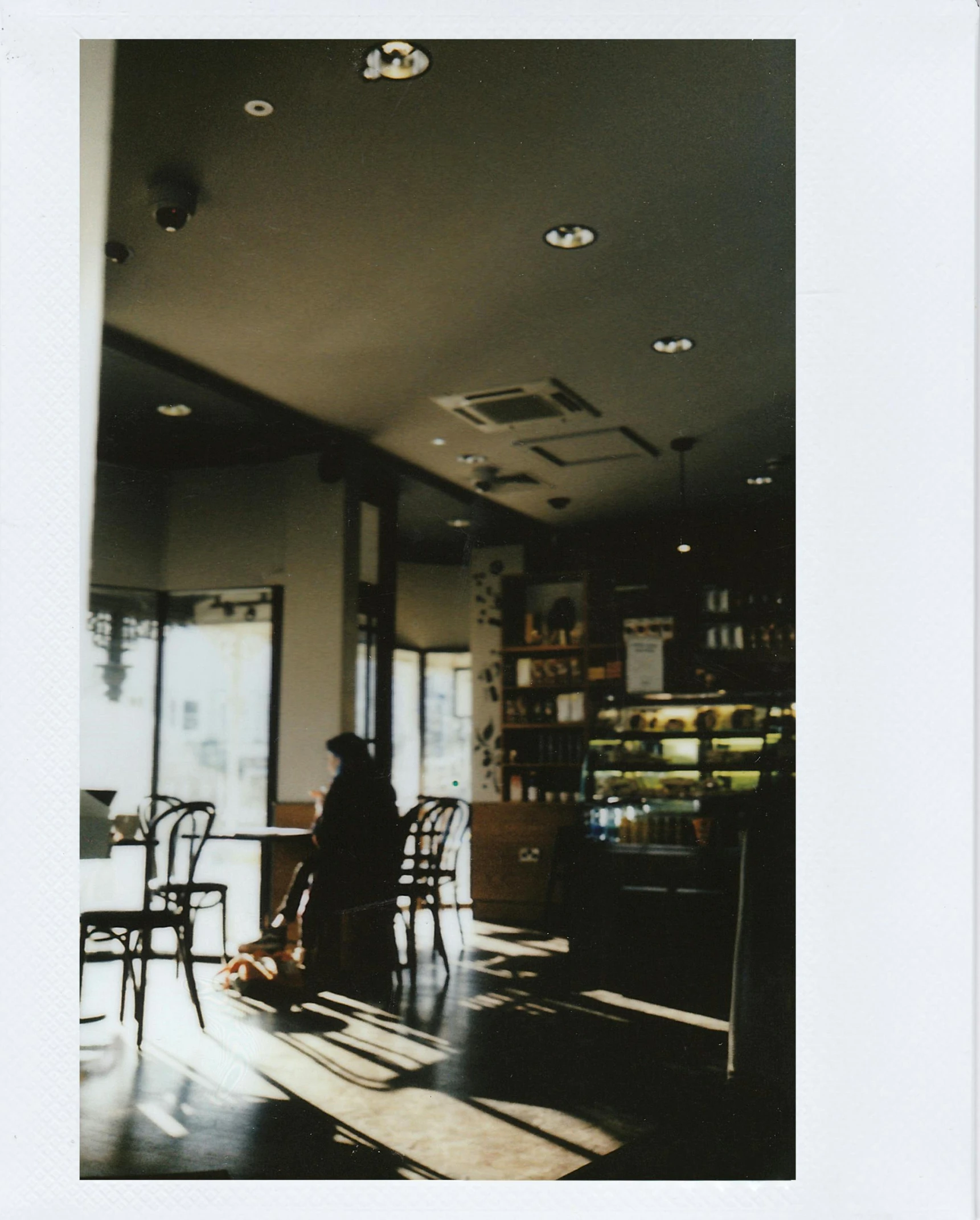 a person sitting at a table in a room, a polaroid photo, by Yasushi Sugiyama, unsplash, cafe interior, sakimichan, alone!!, wide full body