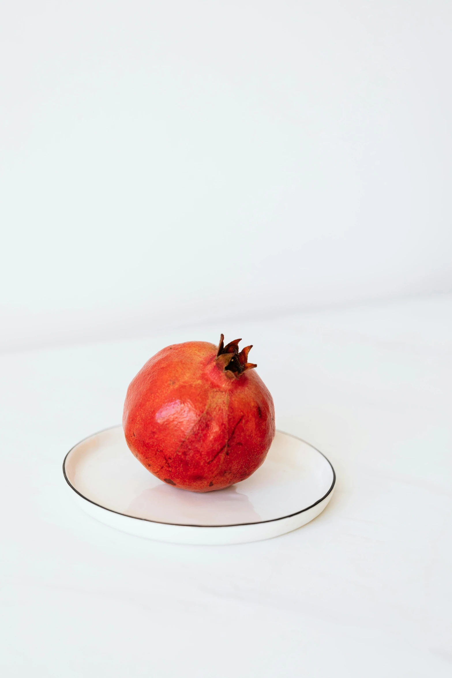 a pomegranate sitting on a plate on a white surface, by Nina Hamnett, trending on unsplash, fine art, natural soft rim light, side front view, large tall, soft vinyl