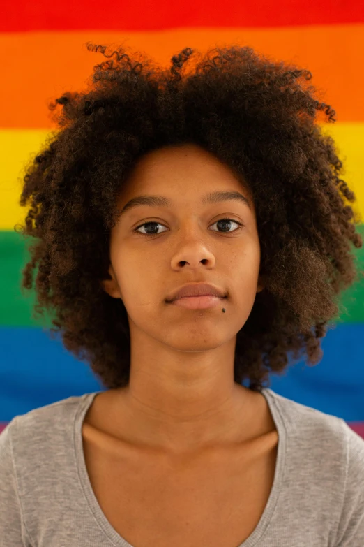 a woman standing in front of a rainbow flag, by Lily Delissa Joseph, black teenage boy, close - up face, curly haired, high quality photo