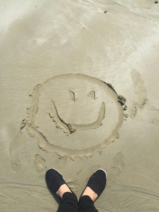 a person standing on a beach with a smiley face drawn in the sand, smileeeeeee, oceanside, on a canva, sitting down