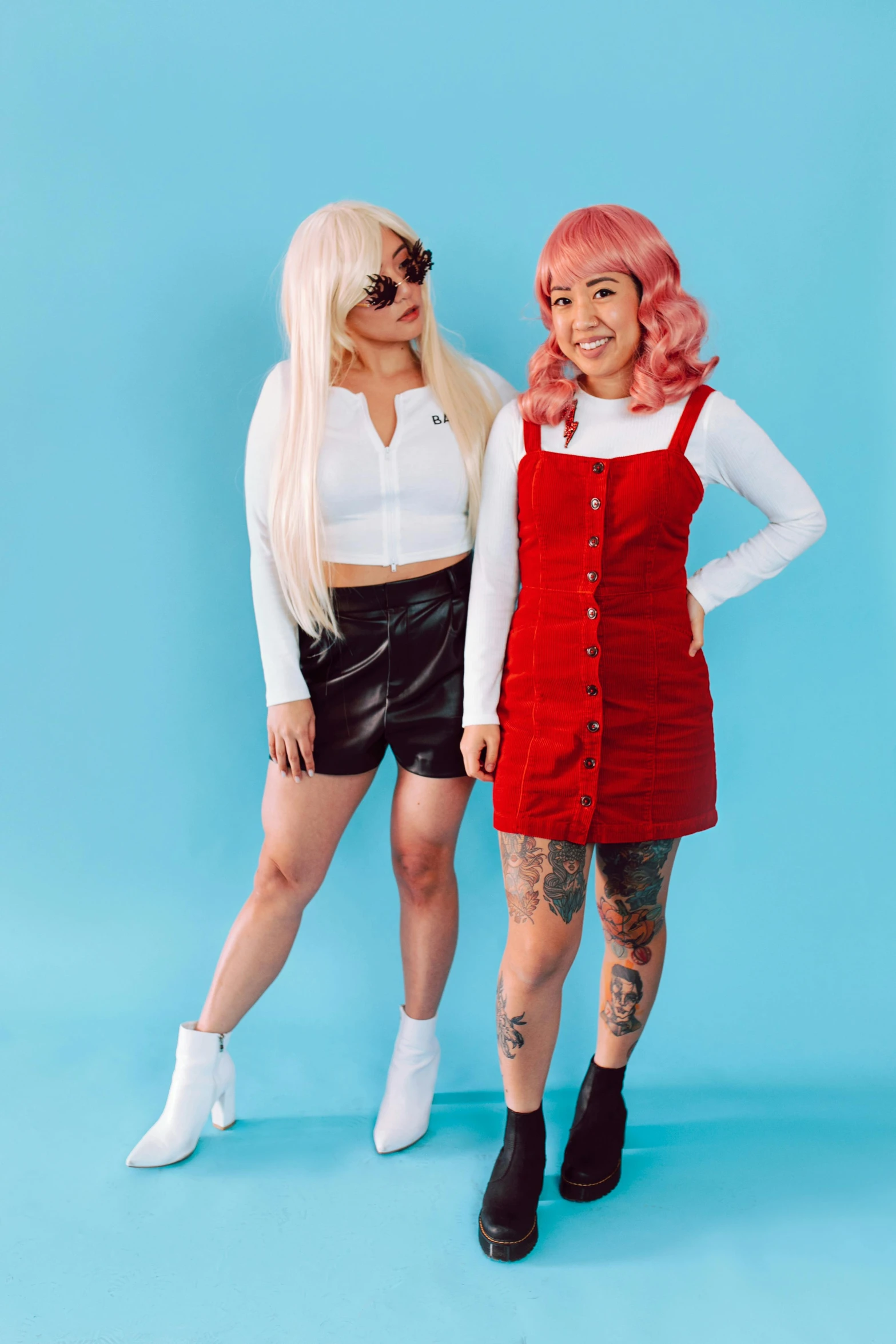 two women standing next to each other on a blue background, inspired by Wang Duo, trending on pexels, international gothic, wearing red shorts, bright white hair, wearing overalls, hot topic