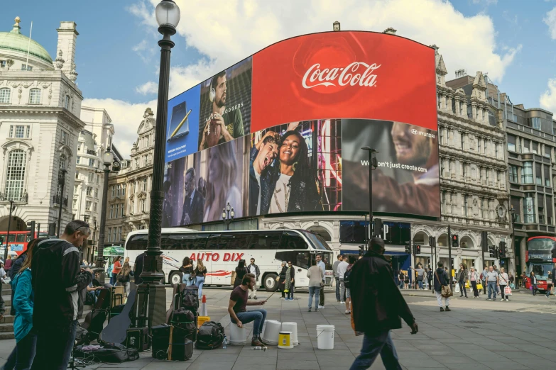 a large coca cola advertisement on the side of a building, a photo, by Emma Andijewska, trending on unsplash, london streets in background, square, people watching around, large screen