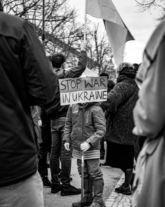 a person holding a sign that says stop war in ukraine, a black and white photo, by Matija Jama, pexels, socialist realism, square, kid, brown, an angry