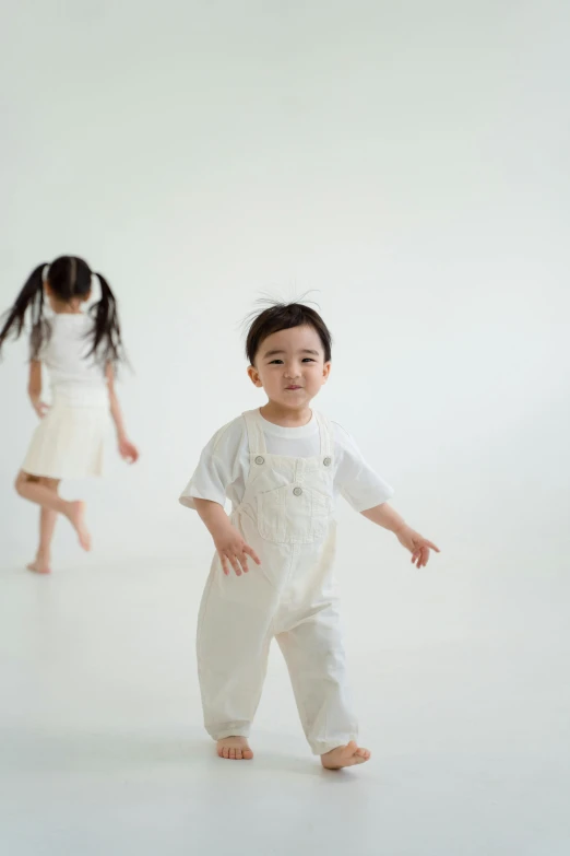 a couple of young children standing next to each other, inspired by Gong Kai, unsplash, gutai group, white studio, wearing overalls, dancing gracefully, japanese collection product