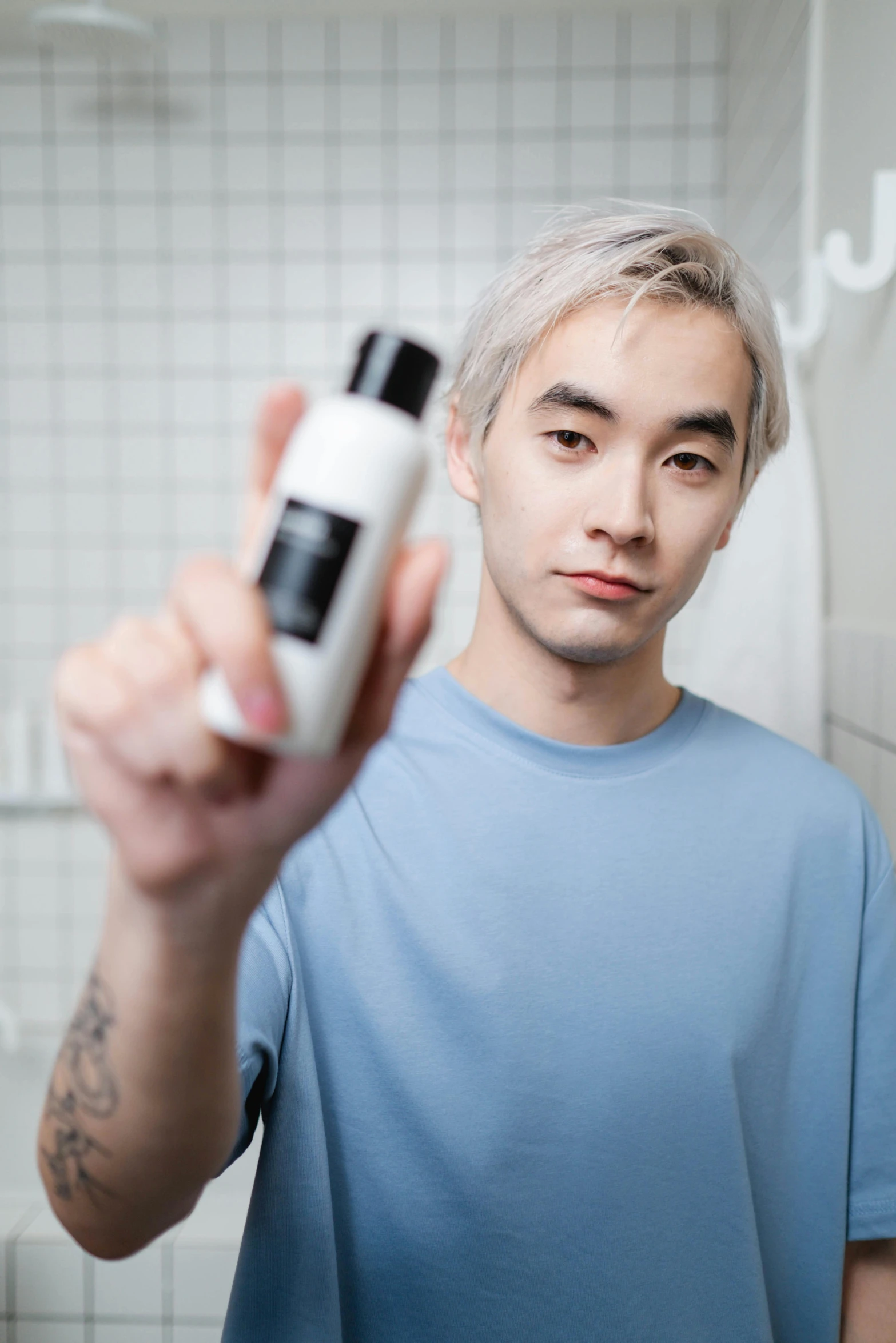 a man holding a bottle of lotion in front of a mirror, inspired by jeonseok lee, platinum hair, looking towards camera, with black, darren quach