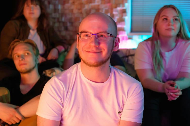 a man sitting in front of a group of people, cute slightly nerdy smile, rave otufit, avatar image, sam leach