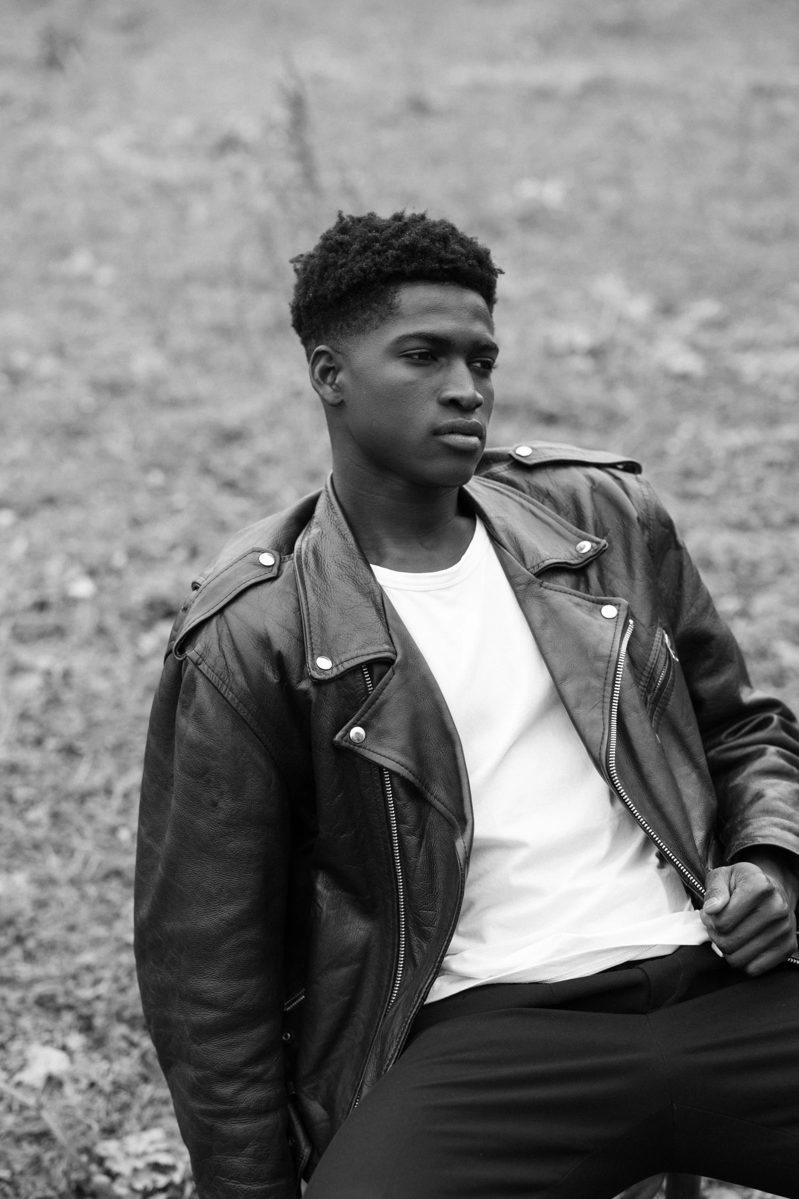 a black and white photo of a man in a leather jacket, by Maxwell Bates, black teenage boy, dark skin tone, hillside, smooth background