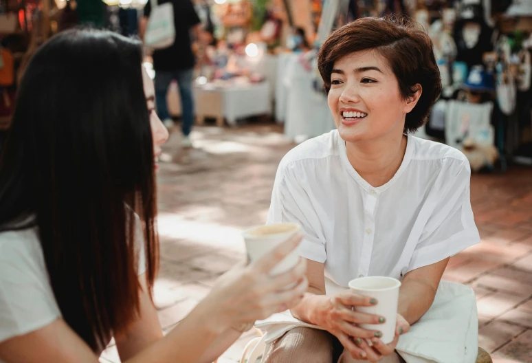 a couple of women sitting next to each other, pexels contest winner, happening, bangkok townsquare, with a white mug, npc talking, maggie cheung