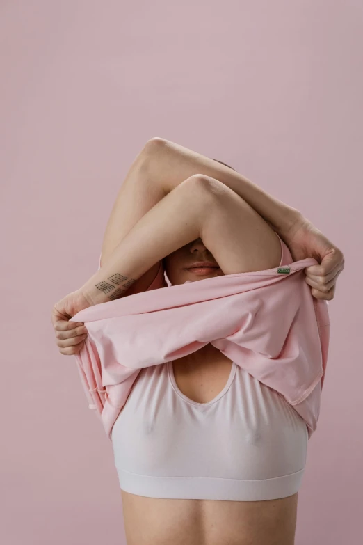 a woman holding a pink shirt over her head, unsplash, happening, breasts covered and sfw, covered with blanket, plain background, contorted