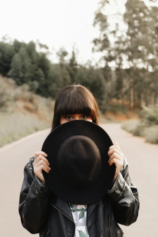 a woman holding a black hat over her face, pexels contest winner, roadside, instagram post, plain background, brunette