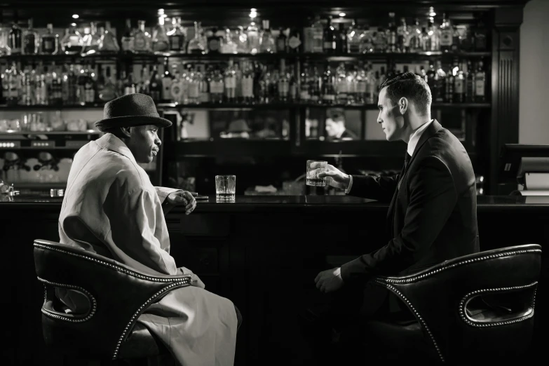 two men sitting at a bar talking to each other, inspired by Peter Lindbergh, unsplash, harlem renaissance, pulp noir, a suited man in a hat, ( ( theatrical ) ), erwin olaf