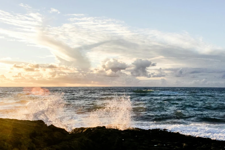 a man standing on top of a rock next to the ocean, unsplash, happening, kauai springtime, waves and splashes, golden hour photo, panoramic shot