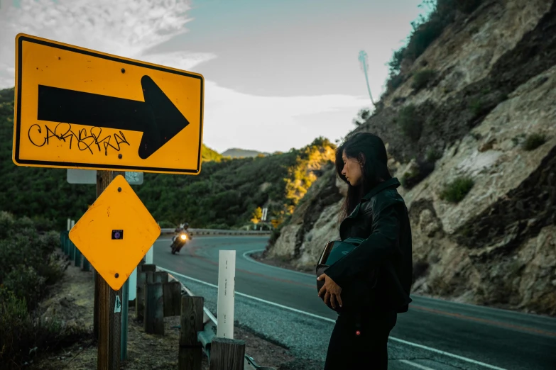 a woman standing on the side of a road next to a road sign, unsplash, realism, point break, post malone, new zealand, avatar image