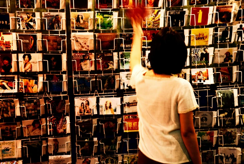 a person standing in front of a wall full of pictures, an album cover, pexels, happening, stood in a supermarket, hands reaching for her, cd, in 2 0 0 2