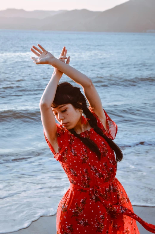 a woman in a red dress standing on a beach, an album cover, inspired by Li Di, unsplash, arabesque, waving hands, young asian woman, oona chaplin, photo of young woman