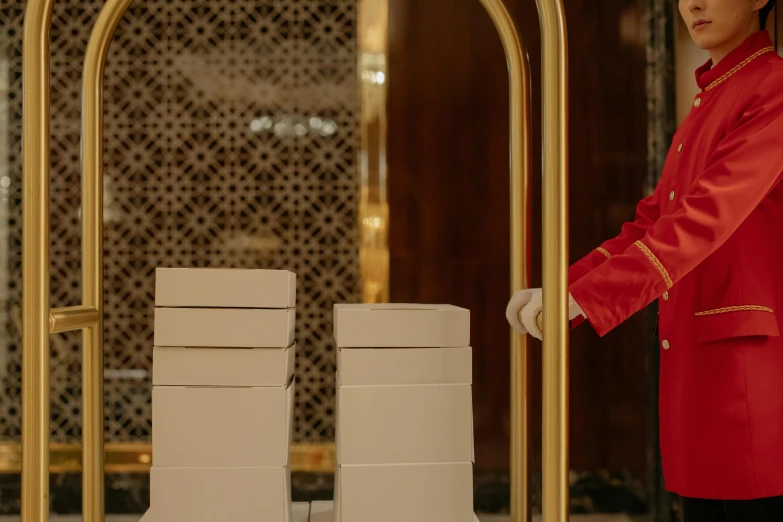 a woman in a red jacket standing next to stacks of boxes, a marble sculpture, by Julia Pishtar, pexels contest winner, michelin star restaurant, white and gold robes, carrying a tray, ( ( theatrical ) )