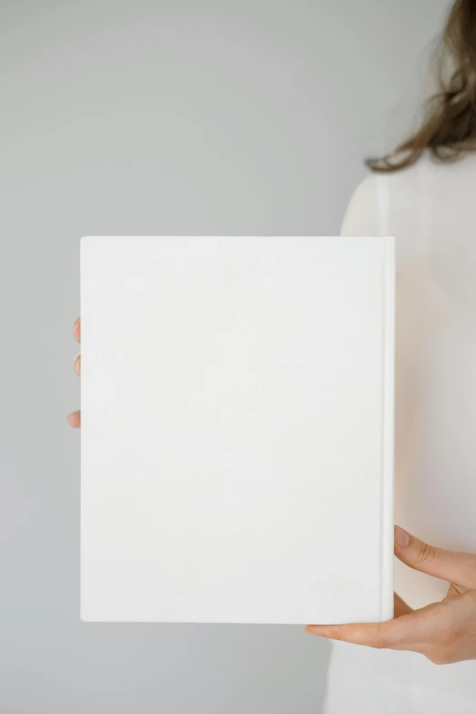 a woman holding a white book in her hands, a minimalist painting, by Carey Morris, trending on unsplash, glossy white metal, vertical orientation, product introduction photo