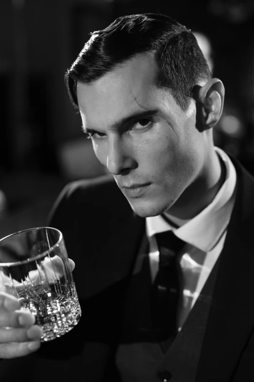 a man in a suit holding a glass of water, a black and white photo, inspired by Yousuf Karsh, bauhaus, benedict cumberbatch, with high cheekbones, promotional image, bartending