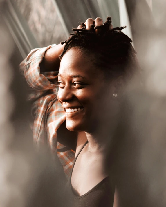 a woman standing in front of a window smiling, by Lily Delissa Joseph, pexels contest winner, happening, in her hair, lupita nyong'o, queer woman, desaturated