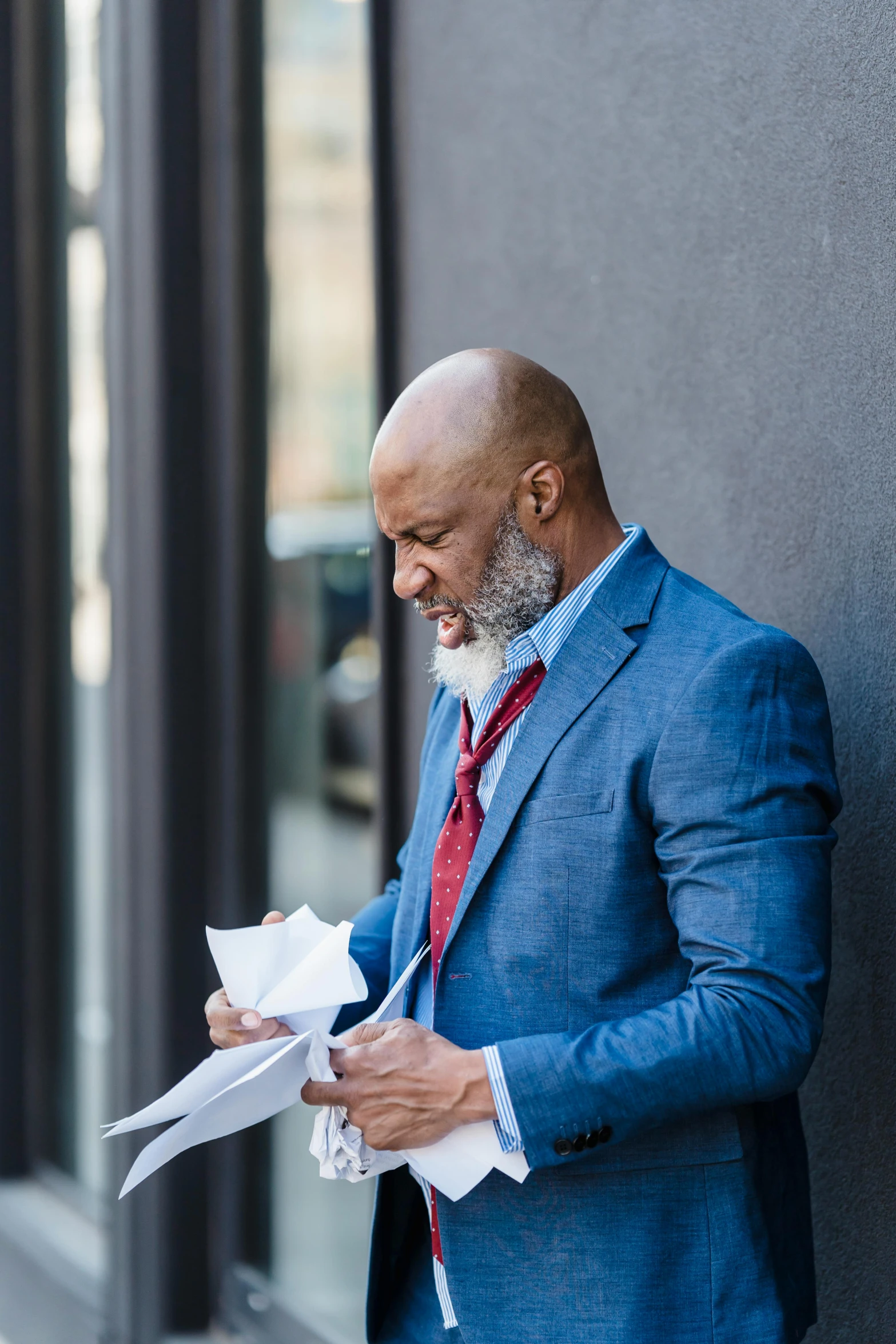 a man in a blue suit holding a piece of paper, a photo, inspired by George Barret, Jr., pexels contest winner, looking away, wearing business casual dress, street life, gray beard