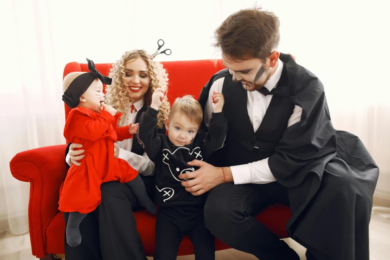 a man sitting on a red couch with two little girls and a man in a tuxedo, pexels contest winner, venom costume, wearing a black catsuit, families playing, andrey surnov