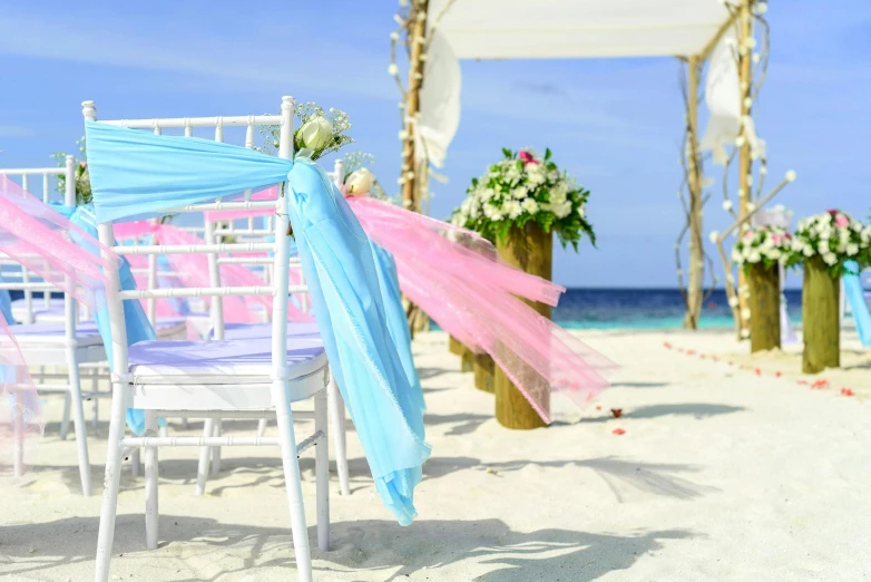 a couple of chairs sitting on top of a sandy beach, flower decorations, pink and blue, white and pink cloth, multiple stories