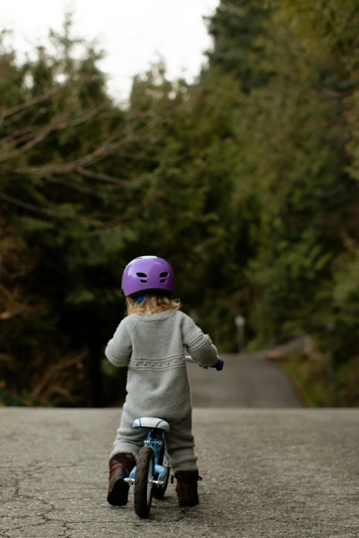 a little boy riding a bike down a road, by Tom Bonson, unsplash, wearing a purple cap, new zealand, toys, girl walking on cliff