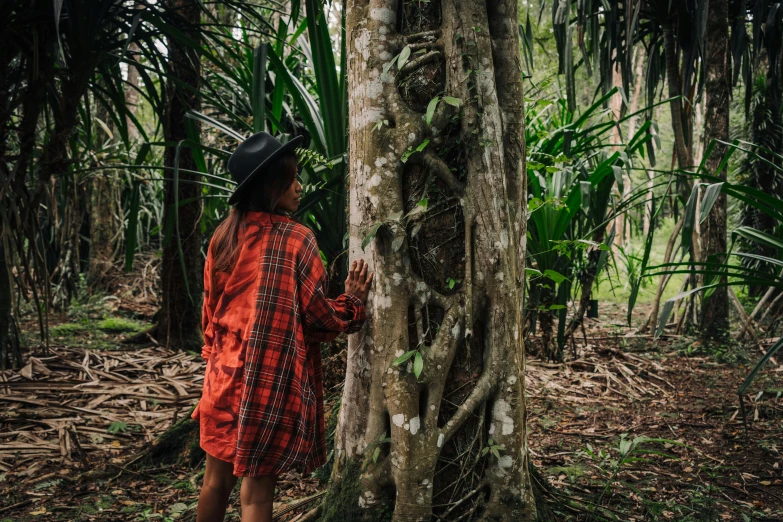 a person standing next to a tree in a forest, unsplash, sumatraism, wearing a red plaid dress, reunion island, 🦩🪐🐞👩🏻🦳, wearing dirty travelling clothes