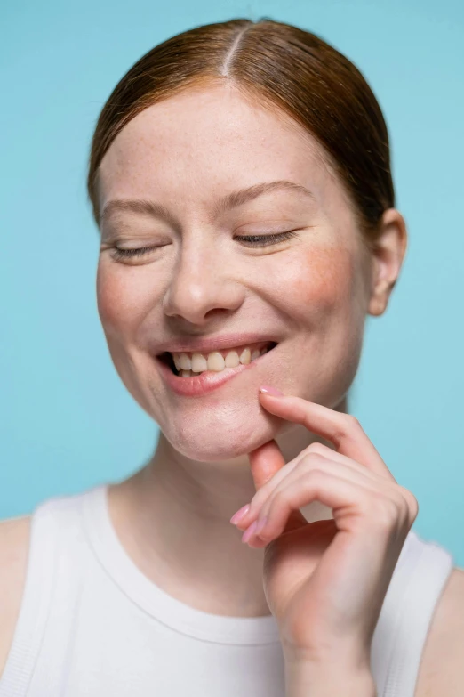 a close up of a person with a tooth brush, winking at the camera, with a blue background, pointé pose;pursed lips, rosy cheeks with freckles