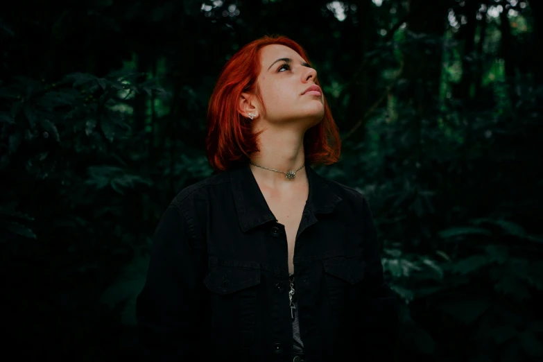 a woman with red hair standing in front of trees, an album cover, inspired by Elsa Bleda, pexels contest winner, realism, looking from side, wearing a black shirt, profile image, in jungle