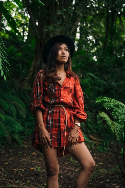 a woman standing in the middle of a forest, an album cover, by Julia Pishtar, sumatraism, wearing a plaid shirt, malaysia jungle, red dress and hat, 5 0 0 px models