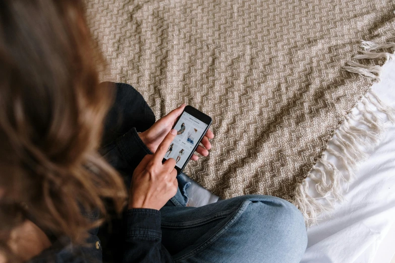 a woman sitting on a bed holding a cell phone, trending on pexels, wearing jeans, instagram post, rectangle, high resolution image
