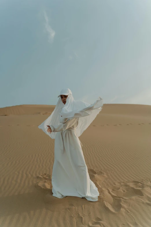 a man standing in the middle of a desert, an album cover, inspired by Amir Zand, pexels contest winner, golden-white robes, cloak covering face, white hijab, ferred - themed robes and hat