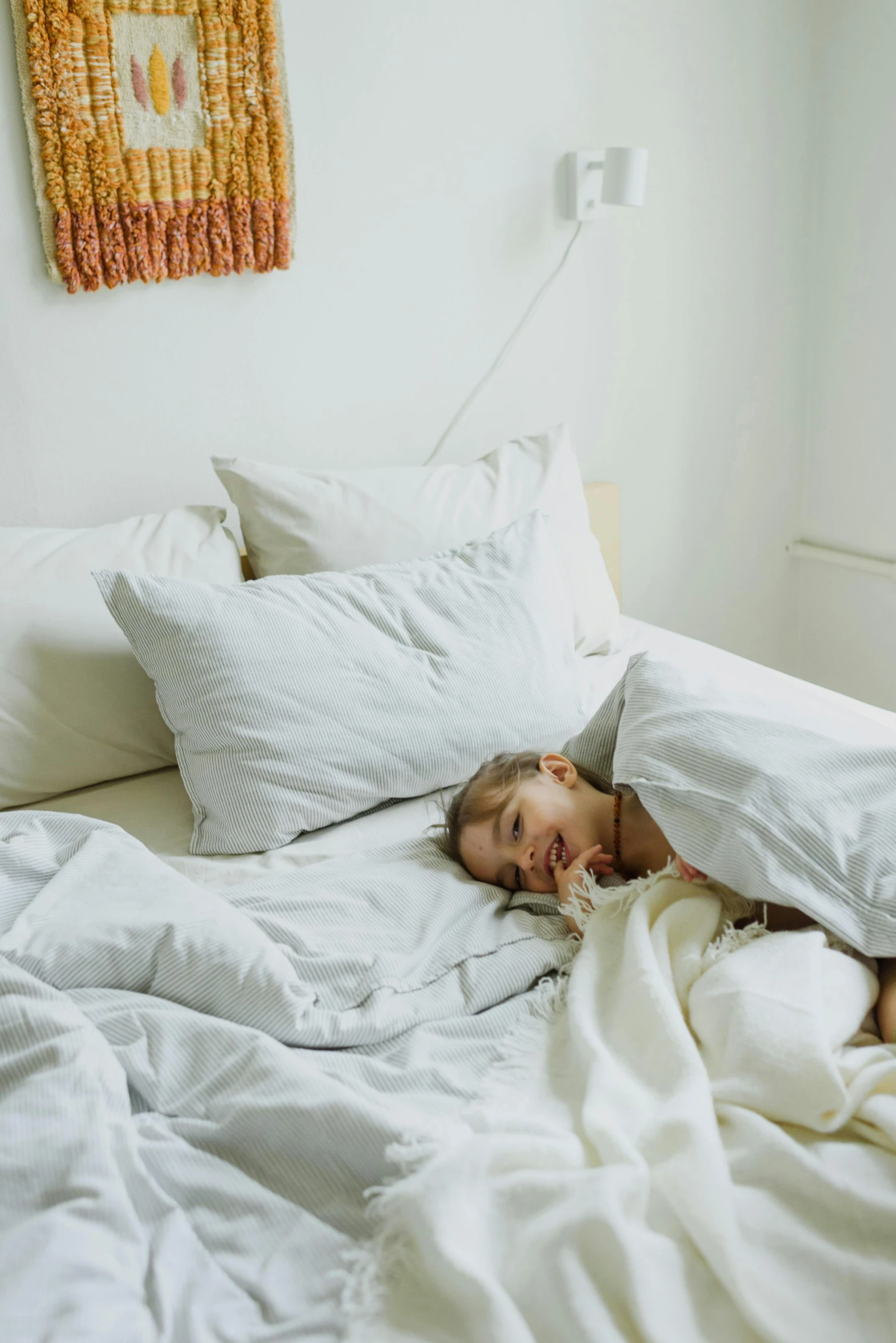 a woman laying on top of a bed covered in white sheets, inspired by Elsa Bleda, visual art, happy kid, looking tired, throw pillows, low quality photo