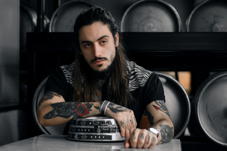 a man with long hair sitting at a table, a tattoo, by Meredith Dillman, pexels contest winner, diego fernandez, turntablist, standing in a restaurant, white metal