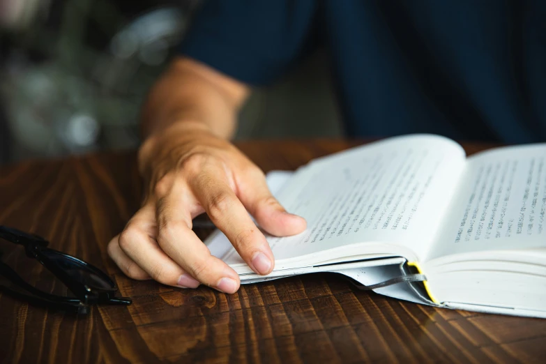 a person sitting at a table reading a book, pexels contest winner, hand on table, maintenance, a handsome, thumbnail