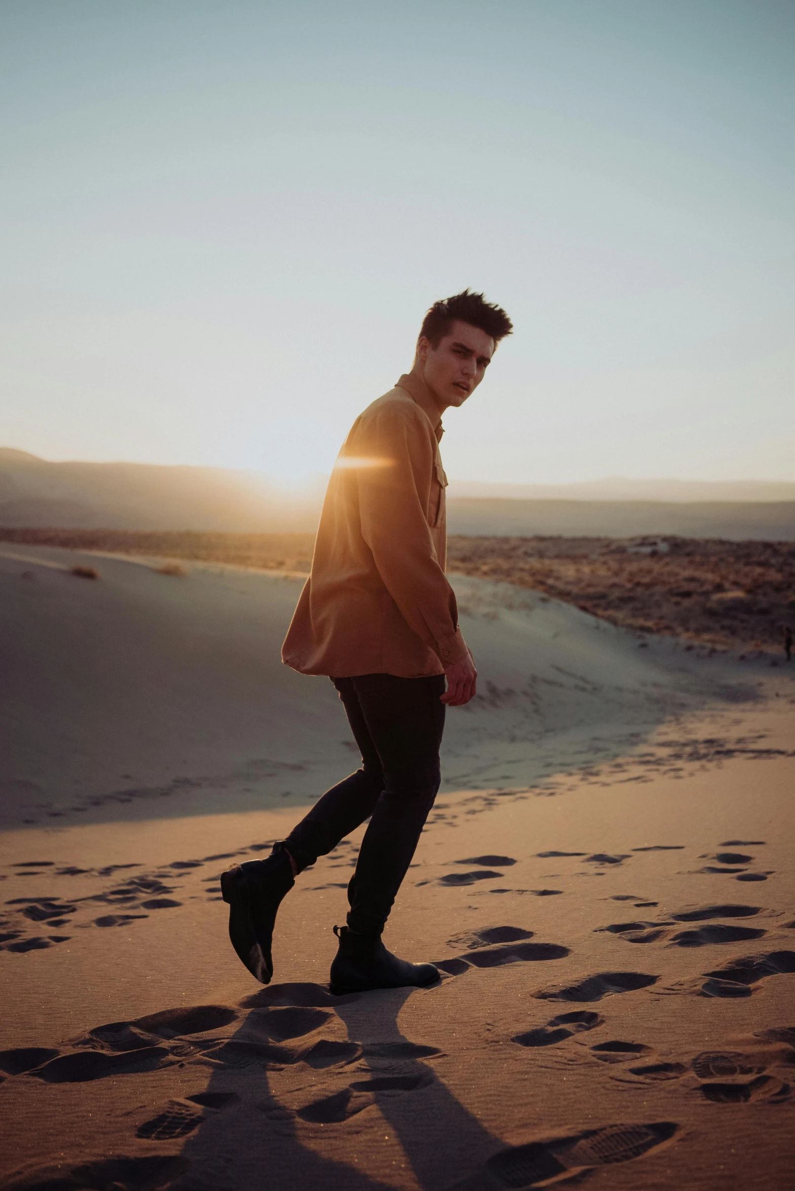 a man walking on top of a sandy beach, an album cover, trending on pexels, andrew garfield, soft golden light, julian ope, model pose