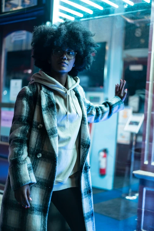 a woman standing in front of a store window, afrofuturism, tartan hoodie, perfectly lit. movie still, with square glasses, at netflix