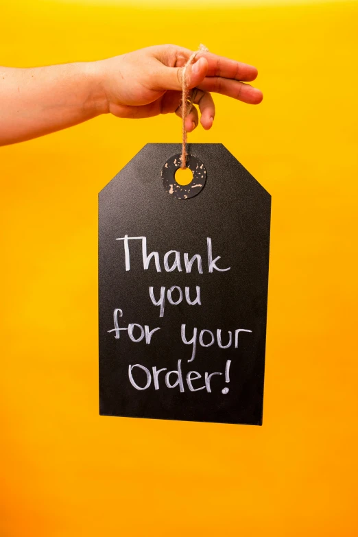 a person holding a tag that says thank you for your order, by Bernie D’Andrea, pexels contest winner, made of smooth black goo, made of glazed, long, amber