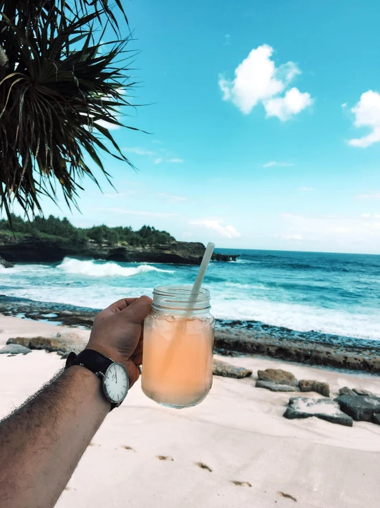 a person holding a glass of orange juice on a beach, a picture, happening, reefs, profile image, watch photo, ocean cliff view