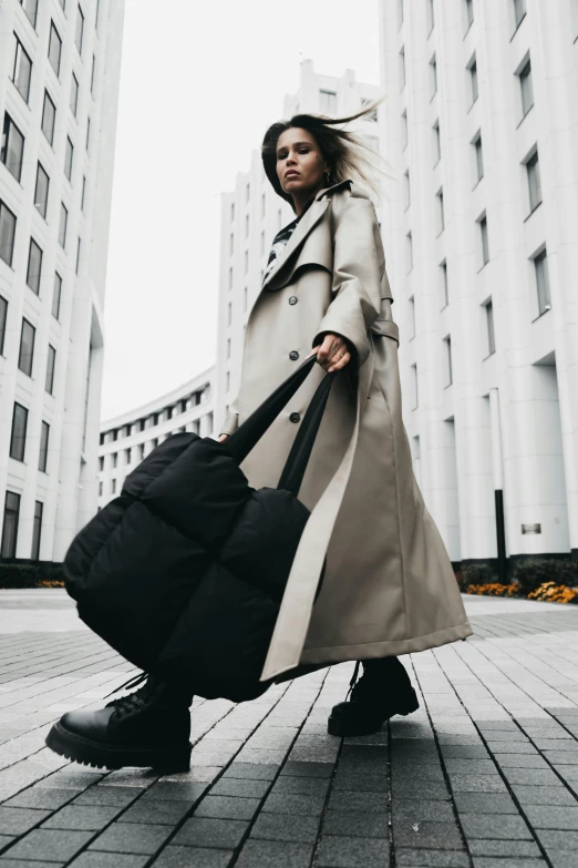 a woman walking down a sidewalk carrying a bag, poster art, by Niko Henrichon, pexels contest winner, wearing a long coat, black. airports, standing on rooftop, puffer jacket