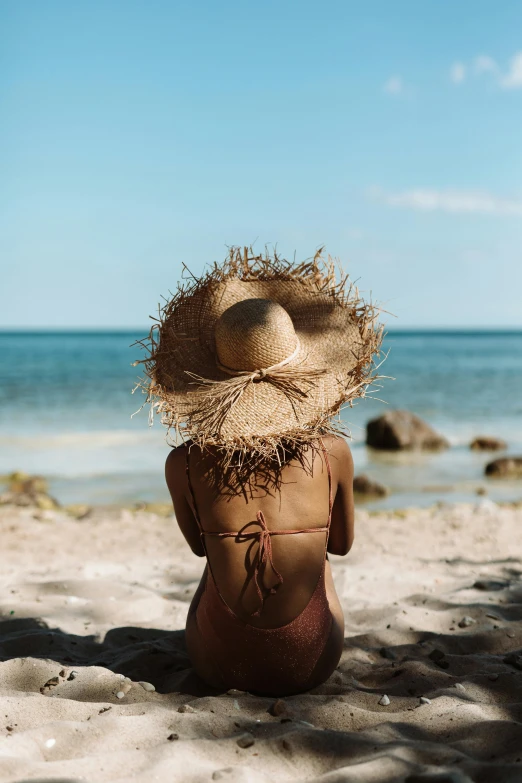 a woman sitting on top of a sandy beach, brown hat, back of head, perfectly shaded body, profile image